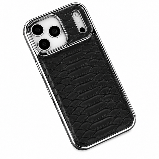 A black snakeskin-patterned phone case lies diagonally against a white background. Irregular raised scale shapes cover the back inside a shiny silver-colored border. A pale three-lens camera panel occupies the upper left, with a separate narrow silver-colored detail containing small round openings beside it.