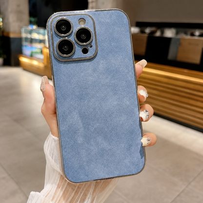 Hand holds a pale blue suede-look case upright in a café. A silver-colored border frames its mottled back and matching camera panel.