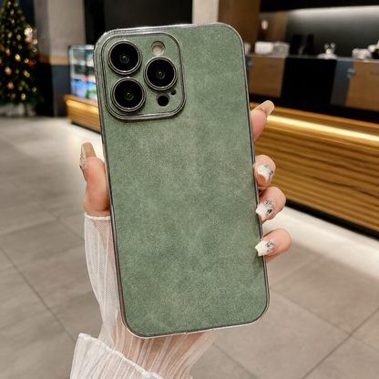 Hand holds a sage green suede-look case upright in a café, showing a mottled plain back and matching camera panel edged in silver color.