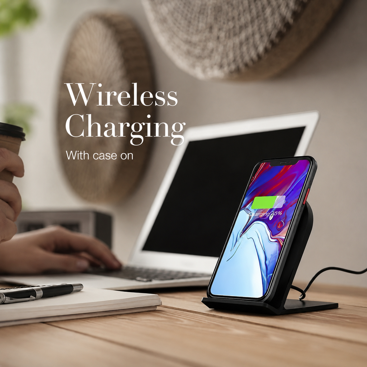 A phone charges upright on a wireless stand beside a laptop on a wooden desk. Text states wireless charging works with the case on.