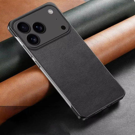 A black leather-look phone case lies diagonally across rolls of black and tan material. Its finely textured back has a broad raised black camera panel and exposed silver-colored side sections.