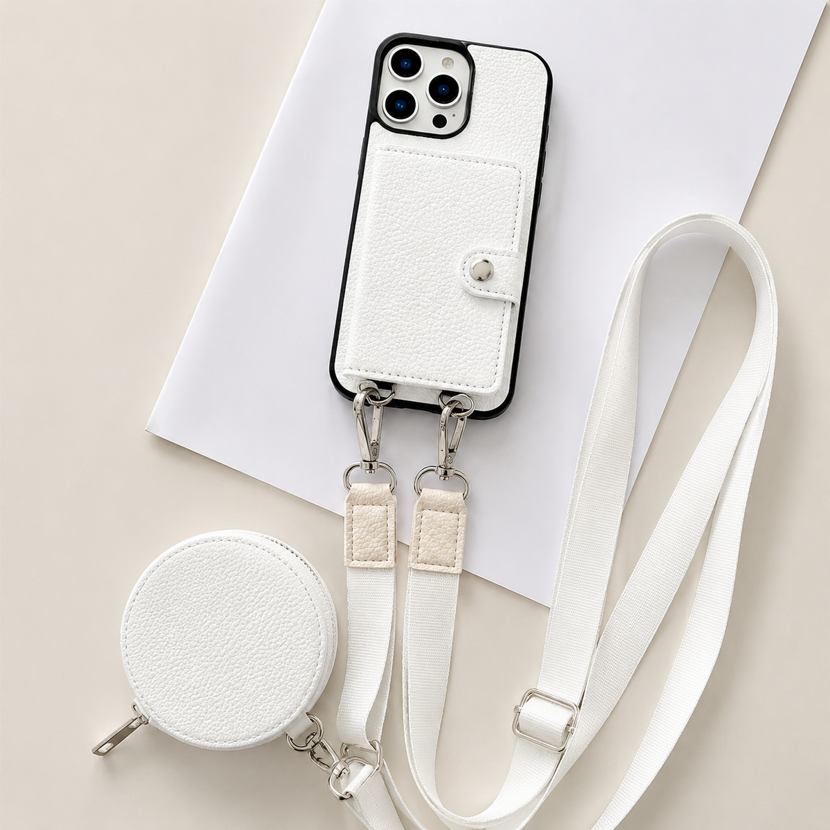 A white textured wallet phone case rests on an angled white sheet beside a matching round zippered pouch and long adjustable strap. A stitched card flap with a silver-colored snap covers the rear. Metal clips connect the strap to two loops on the phone's lower edge, with pale fabric sections near the clips.