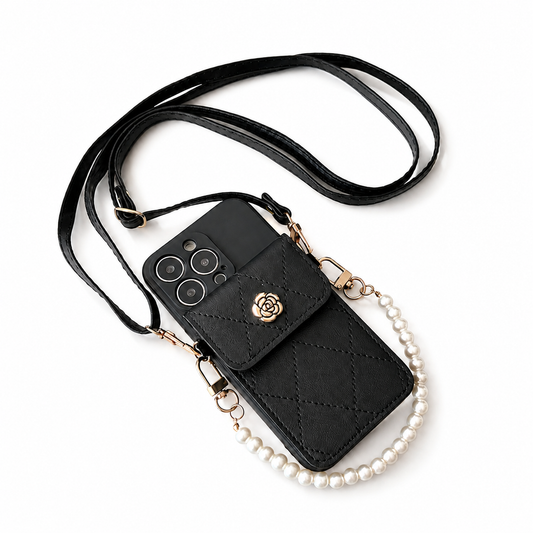 A black quilted phone wallet lies diagonally on a pale surface beside its long matching shoulder strap. Diamond stitching covers the rear pocket, which closes with a flap and gold rose-shaped ornament. A short strand of pearl-like white beads attaches to gold clips at the sides, forming a small carrying handle.