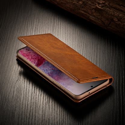 A tan wallet lies partly open over a phone on dark wood. The pink-patterned screen peeks beneath the stitched front flap, with charging openings visible below.