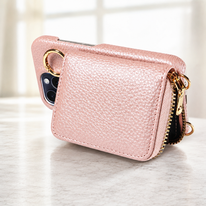 A pale pink pebbled wallet phone case rests sideways on a light countertop. Its rectangular back pouch, gold-colored zipper and ring fitting are visible beside the camera opening.