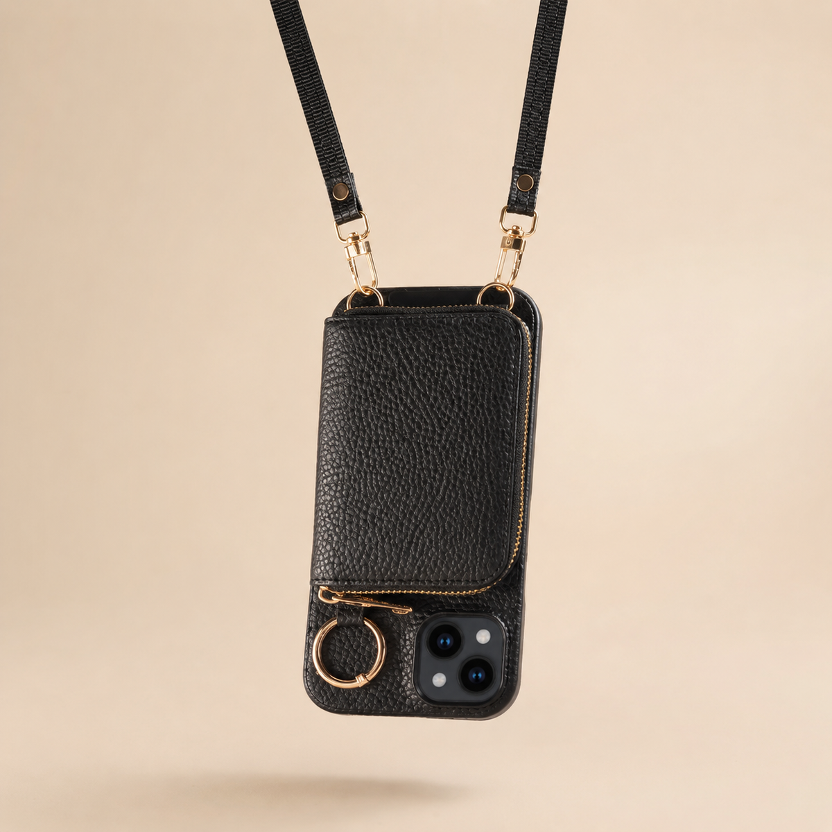 A black textured wallet phone case hangs from a long strap against beige. Gold-colored clips attach at the top, while the zipper pouch, circular ring and two-lens opening face forward.