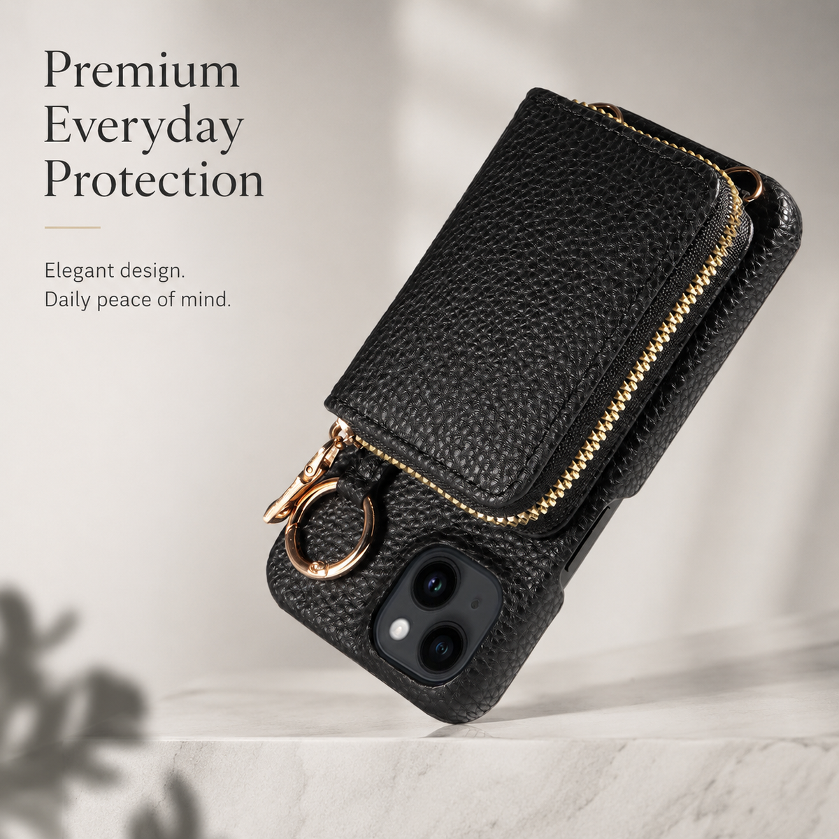 A black pebbled wallet case floats diagonally above a pale ledge. Its rectangular pouch has a gold-colored zipper, with a circular ring beside the two-lens camera opening.