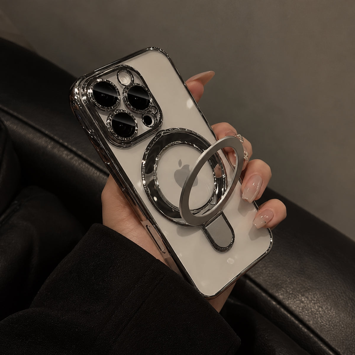A hand holding a white iPhone case with a metallic silver MagSafe ring holder, shown against a dark leather background.
