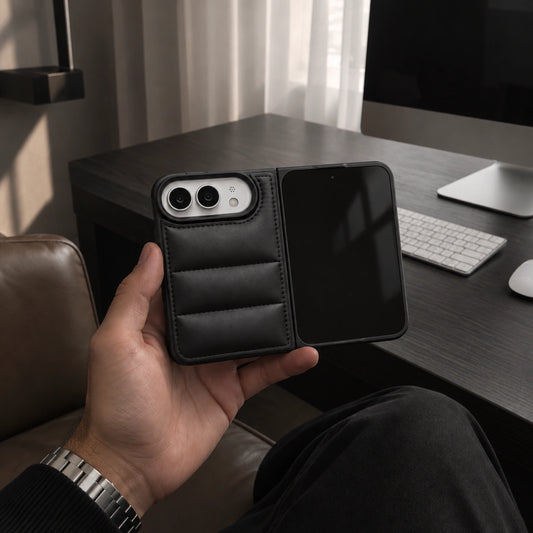 A black leather wallet-style phone case with a card slot and padded interior, held in a person's hand in an office setting near a desk and computer.