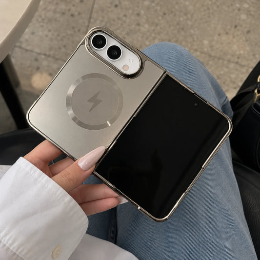A person holding a metallic silver flip phone case with a circular magnetic ring design, shown in a lifestyle setting with blue jeans and a white shirt visible.